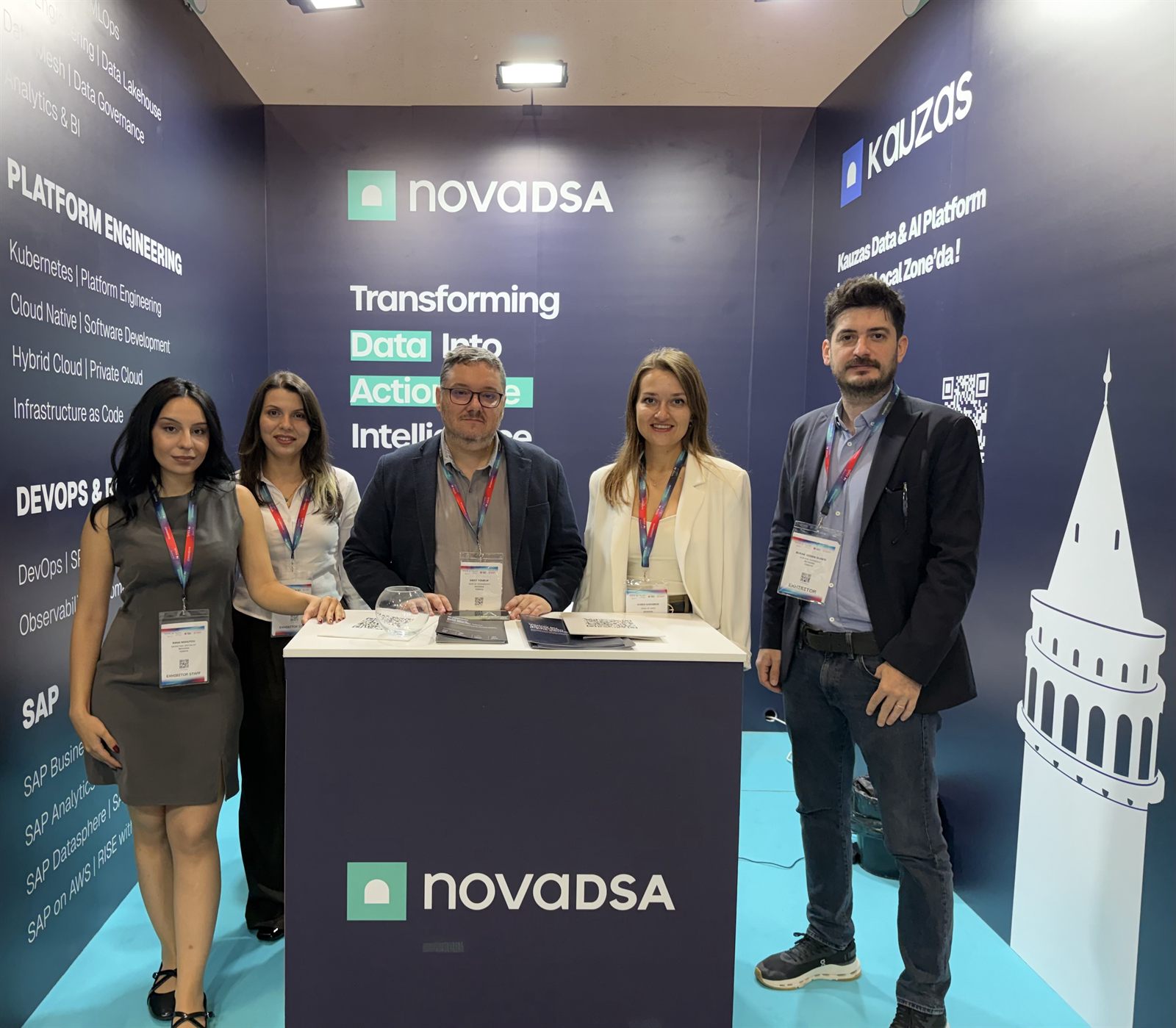 Novadsa ekibi Gitex AI 2026 standında. Duvarlarda Kauzas logosu, platformun kapsadığı başlıklar ve Galata Kulesi çizimi var.